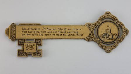 市鑰背面。右側匙柄部位圖案為舊金山市政廳，匙身上有第28任市長Edward Robeson Taylor銘記在市政廳內的文字。